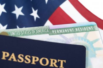 United States of America permanent resident card, green card, displayed with a US flag in the background and a passport in the foreground. Immigration concept.