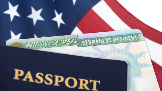 United States of America permanent resident card, green card, displayed with a US flag in the background and a passport in the foreground. Immigration concept.